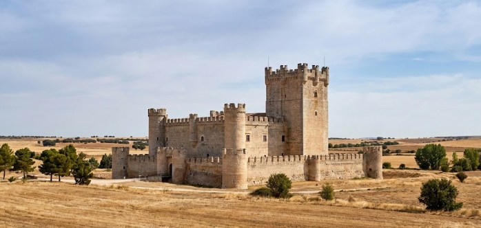 Impresionante vista frontal de un castillo medieval en la provincia de Valladolid, destacando sus torres almenadas y muros de piedra bajo un cielo despejado.