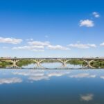 Puente Nuevo de Zamora o Puente de los Poetas cruzando el río Duero con reflejos en el agua bajo un cielo azul.