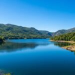 Vista panorámica del Lago de Sanabria en un día soleado, con aguas azules cristalinas rodeadas de montañas verdes y bosques frondosos.